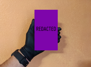 Male hand model with black glove, holding a REDACTED purple box, in front of a wall, wearing a watch